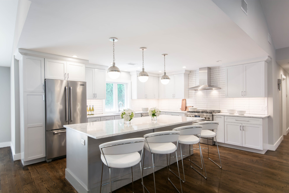 Photo of a large modern l-shaped open plan kitchen in Providence with an undermount sink, shaker cabinets, white cabinets, white splashback, ceramic splashback, stainless steel appliances, dark hardwood floors, with island, brown floor, white benchtop and quartz benchtops.