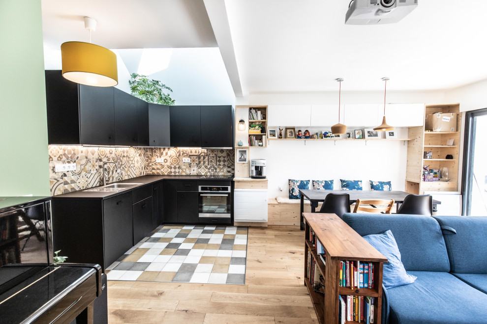 Design ideas for a contemporary l-shaped open plan kitchen in Bordeaux with a drop-in sink, flat-panel cabinets, black cabinets, multi-coloured splashback, stainless steel appliances, multi-coloured floor and black benchtop.