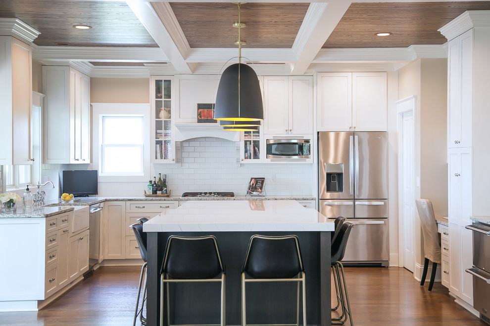 Photo of a large transitional u-shaped separate kitchen in Milwaukee with a farmhouse sink, quartz benchtops, white splashback, subway tile splashback, stainless steel appliances, medium hardwood floors, with island, white benchtop, shaker cabinets, white cabinets and brown floor.