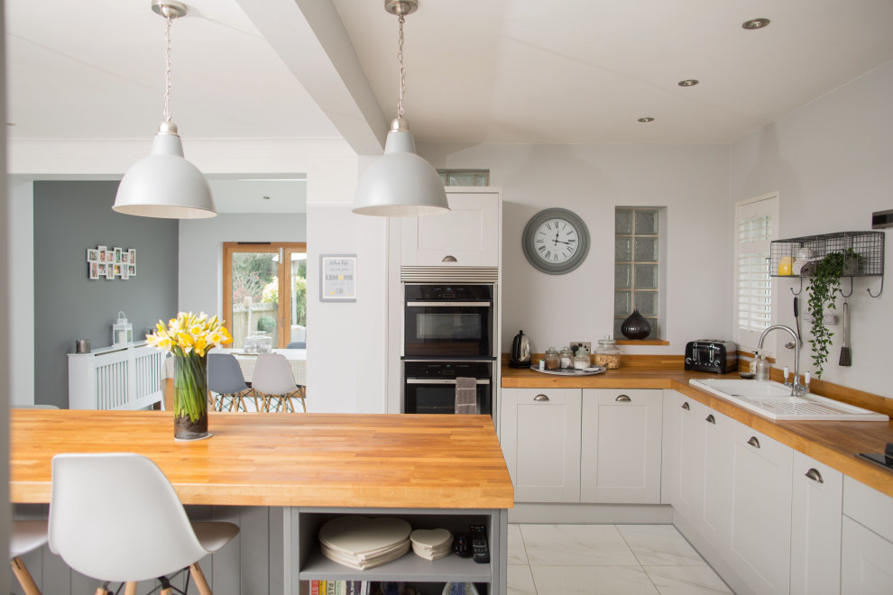 Photo of a classic u-shaped kitchen/diner in Other with a built-in sink, shaker cabinets, grey cabinets, wood worktops, black appliances, an island, brown worktops and white floors.