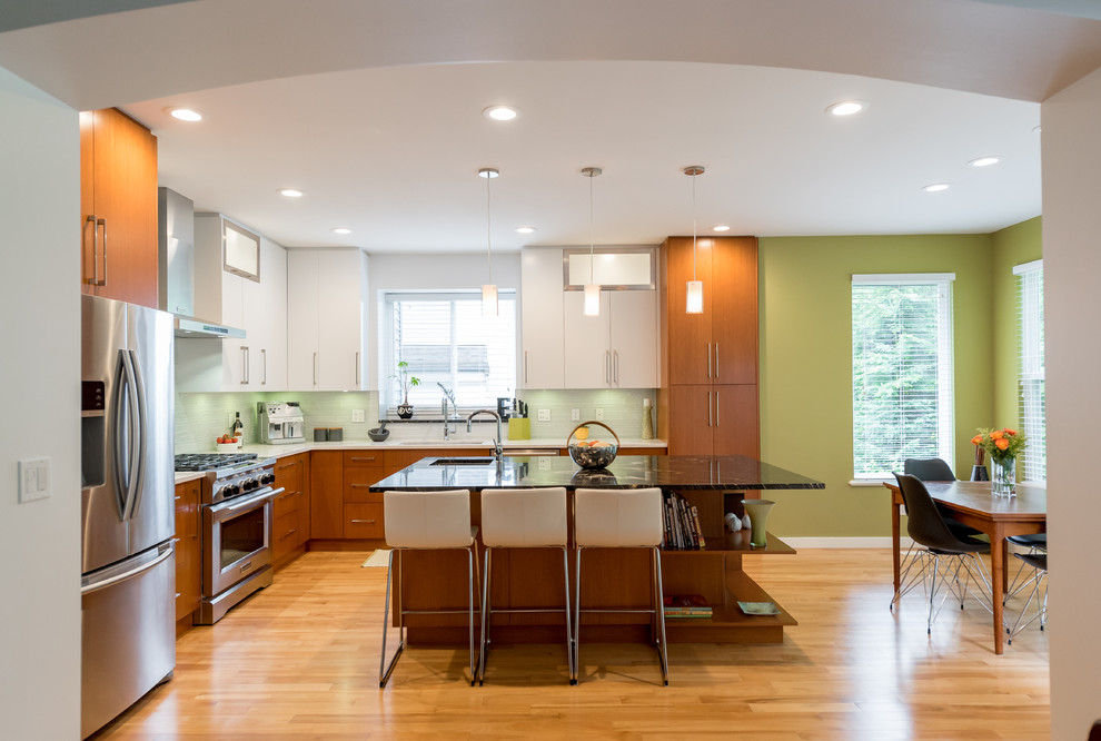 Mid-sized contemporary l-shaped separate kitchen in Vancouver with flat-panel cabinets, medium wood cabinets, granite benchtops, grey splashback, glass tile splashback, stainless steel appliances, light hardwood floors, with island, brown floor and black benchtop.