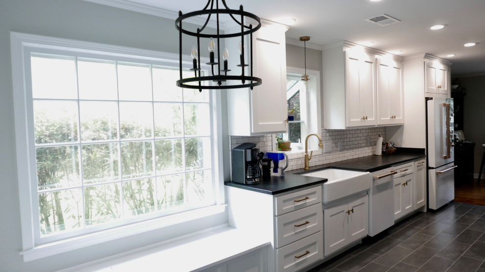 Mid-sized transitional galley porcelain tile and black floor eat-in kitchen photo with a farmhouse sink, shaker cabinets, white cabinets, soapstone countertops, white backsplash, subway tile backsplash, white appliances, an island and black countertops