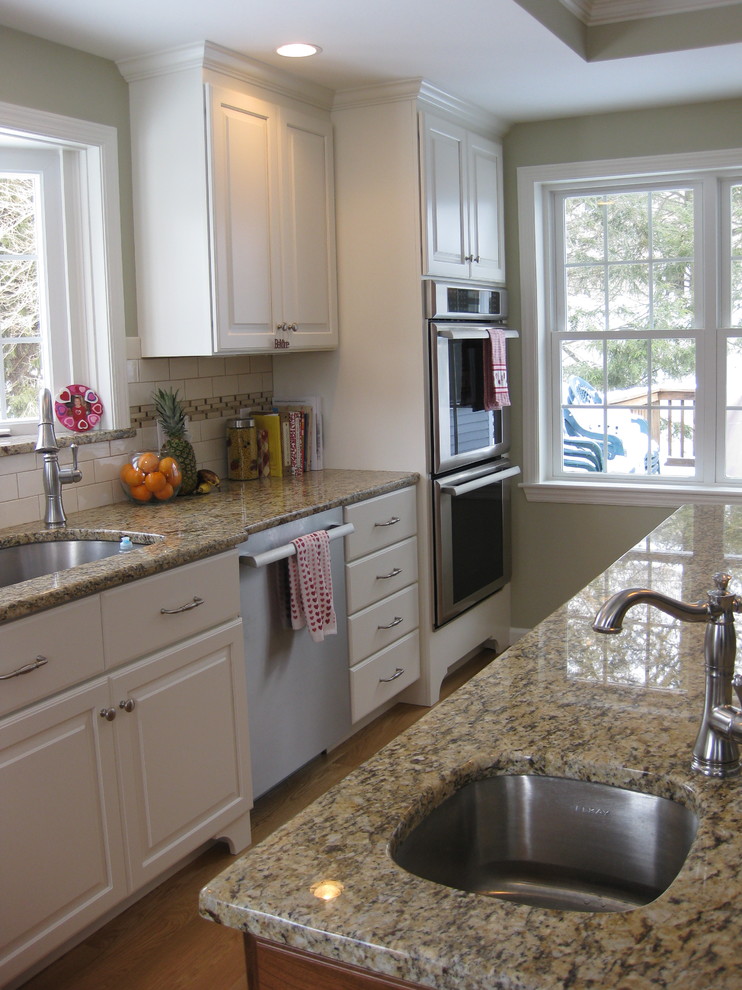 Eat-in kitchen - transitional u-shaped medium tone wood floor eat-in kitchen idea in Boston with an undermount sink, raised-panel cabinets, white cabinets, granite countertops, white backsplash, ceramic backsplash, stainless steel appliances, an island and beige countertops