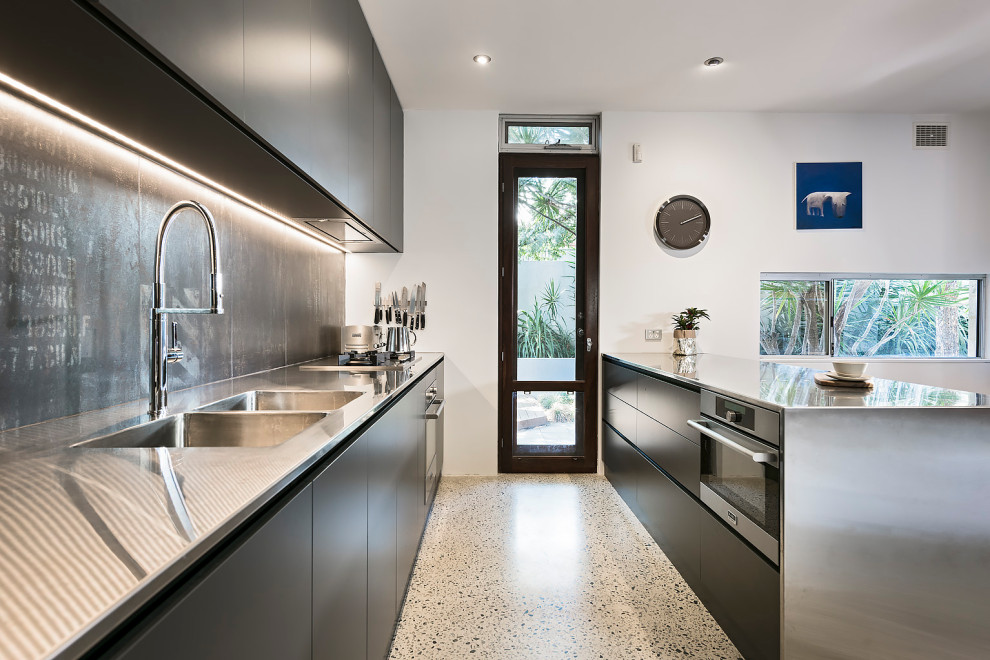 Inspiration for a mid-sized industrial galley eat-in kitchen in Perth with an integrated sink, flat-panel cabinets, black cabinets, stainless steel benchtops, black splashback, porcelain splashback, stainless steel appliances, concrete floors, with island, grey floor and grey benchtop.