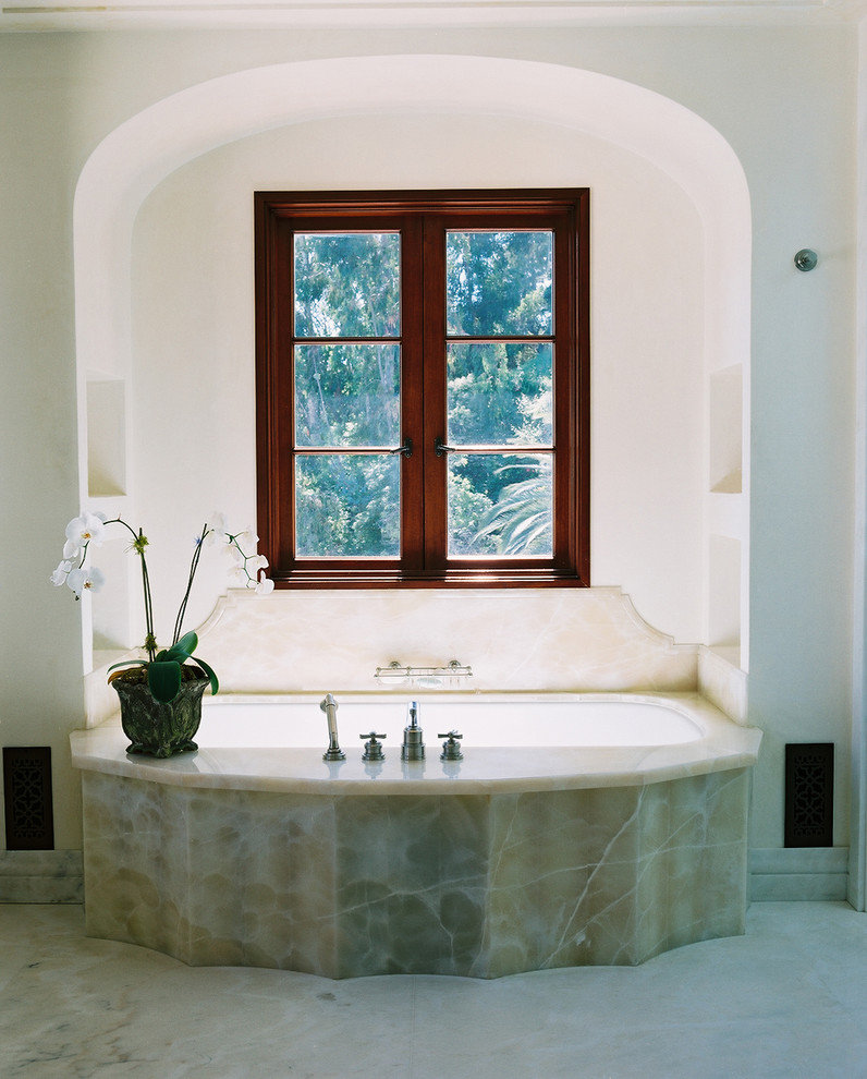 Inspiration for a mediterranean bathroom in Los Angeles with an undermount tub, stone slab and beige tile.