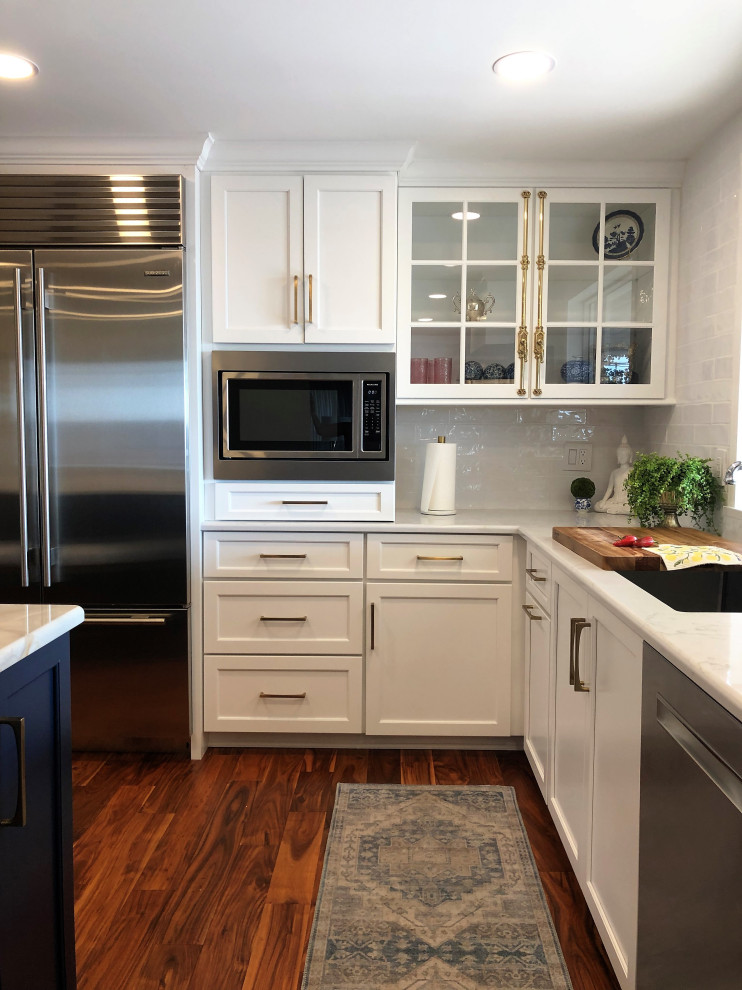 Mid-sized transitional l-shaped medium tone wood floor and brown floor kitchen pantry photo with an undermount sink, flat-panel cabinets, blue cabinets, quartz countertops, white backsplash, subway tile backsplash, stainless steel appliances, an island and gray countertops