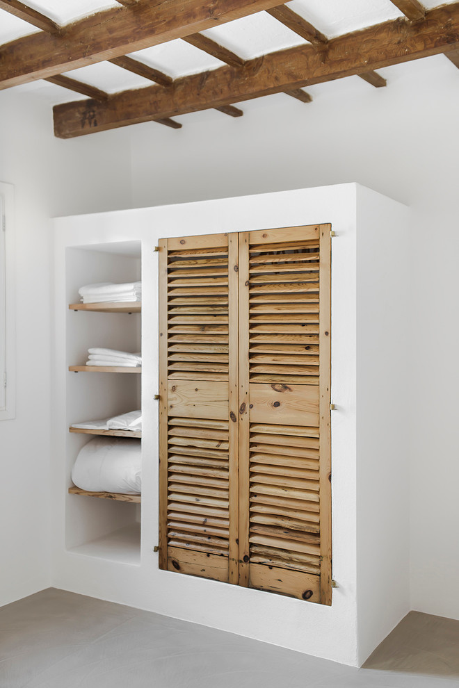 Inspiration for a small mediterranean gender-neutral built-in wardrobe in Barcelona with light wood cabinets, concrete floors and louvered cabinets.