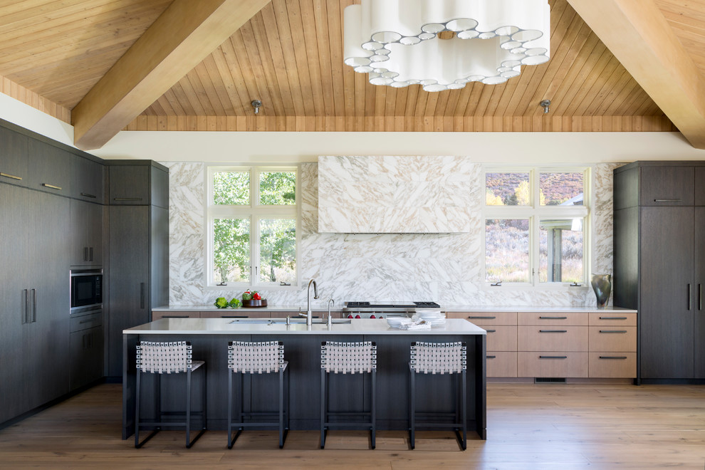 Photo of a contemporary l-shaped open plan kitchen in Denver with an undermount sink, flat-panel cabinets, black cabinets, beige splashback, panelled appliances, light hardwood floors, with island and white benchtop.