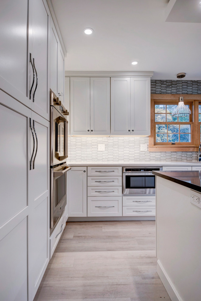 Example of a large transitional u-shaped light wood floor and beige floor open concept kitchen design in New York with an undermount sink, shaker cabinets, white cabinets, quartzite countertops, white backsplash, ceramic backsplash, stainless steel appliances, an island and white countertops