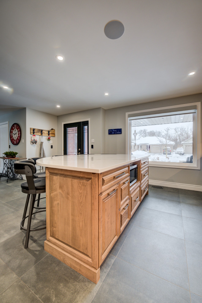 Example of a mid-sized transitional l-shaped eat-in kitchen design in Toronto with an undermount sink, raised-panel cabinets, medium tone wood cabinets, quartz countertops, white backsplash, ceramic backsplash, stainless steel appliances, an island and white countertops