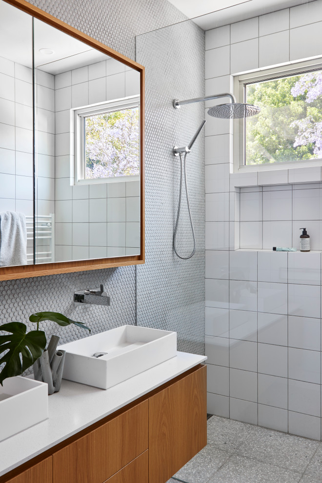 This is an example of a contemporary bathroom in Melbourne with flat-panel cabinets, medium wood cabinets, a curbless shower, white tile, a vessel sink, grey floor, white benchtops, a double vanity and a floating vanity.