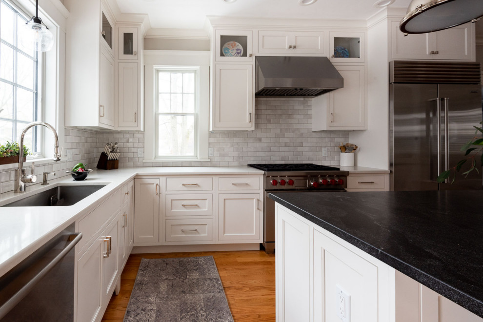 Inspiration for a large transitional u-shaped medium tone wood floor and brown floor eat-in kitchen remodel in Boston with an undermount sink, shaker cabinets, white cabinets, quartz countertops, gray backsplash, subway tile backsplash, stainless steel appliances, an island and black countertops