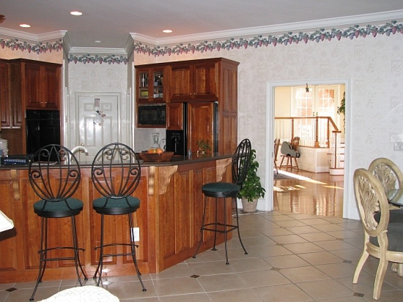 Example of an u-shaped ceramic tile open concept kitchen design with raised-panel cabinets, medium tone wood cabinets, beige backsplash, black appliances and no island