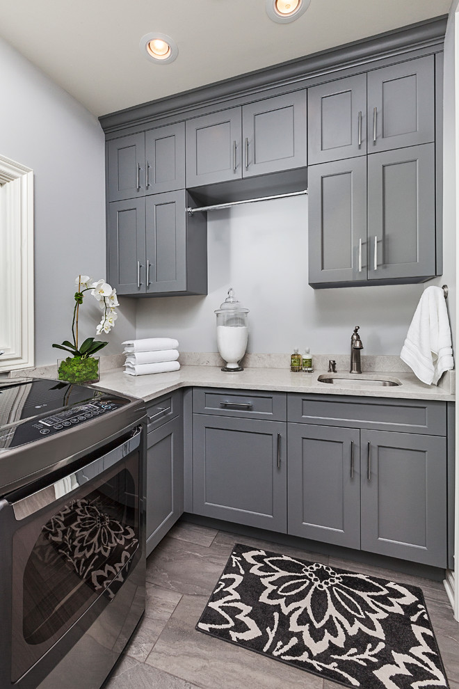 This is an example of a mid-sized transitional l-shaped dedicated laundry room in Detroit with an undermount sink, shaker cabinets, grey cabinets, quartz benchtops, grey walls, porcelain floors and a side-by-side washer and dryer.