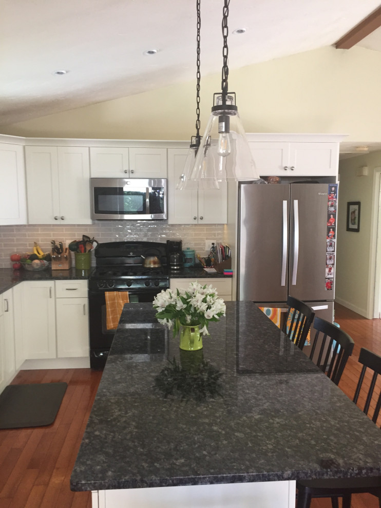 Mid-sized transitional l-shaped open plan kitchen in Boston with a double-bowl sink, shaker cabinets, white cabinets, granite benchtops, grey splashback, ceramic splashback, stainless steel appliances, medium hardwood floors, with island, brown floor and blue benchtop.
