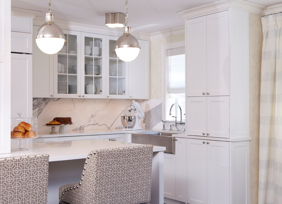 Transitional kitchen in New York with a farmhouse sink, shaker cabinets, white cabinets, white splashback and a peninsula.