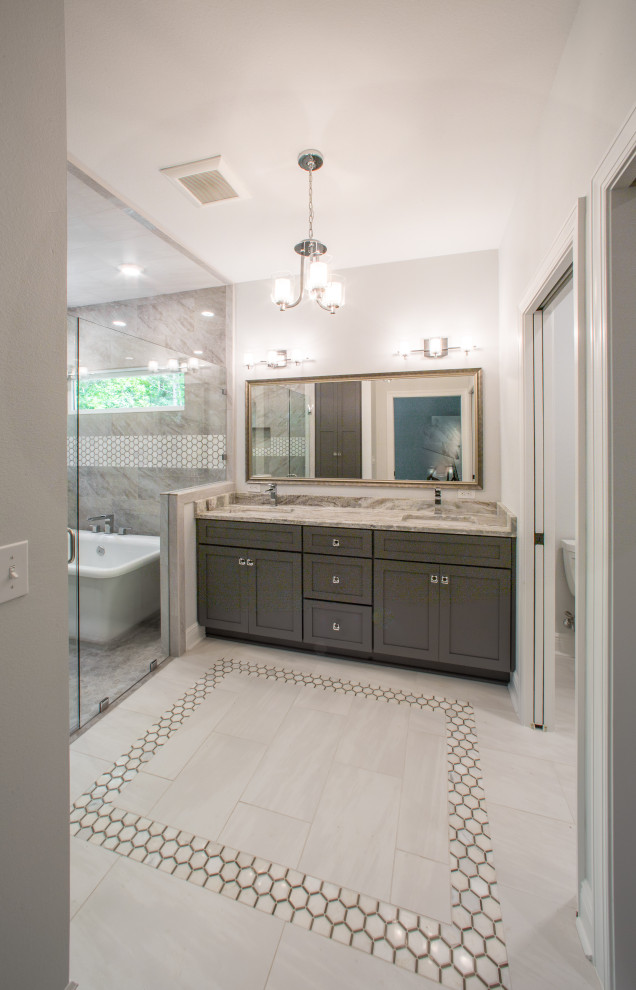 This is an example of a mid-sized traditional master bathroom with a built-in vanity, recessed-panel cabinets, grey cabinets, a freestanding tub, a curbless shower, a one-piece toilet, multi-coloured tile, porcelain tile, white walls, porcelain floors, an integrated sink, quartzite benchtops, white floor, a hinged shower door, multi-coloured benchtops, an enclosed toilet and a double vanity.
