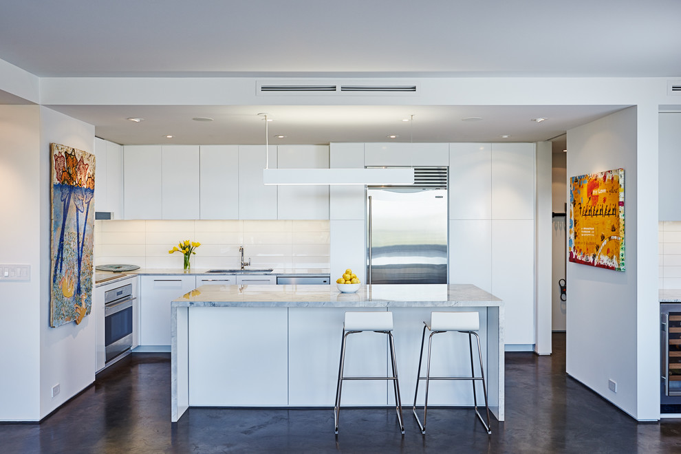 Photo of a contemporary l-shaped kitchen in Houston with an undermount sink, flat-panel cabinets, white cabinets, white splashback, stainless steel appliances, concrete floors and with island.