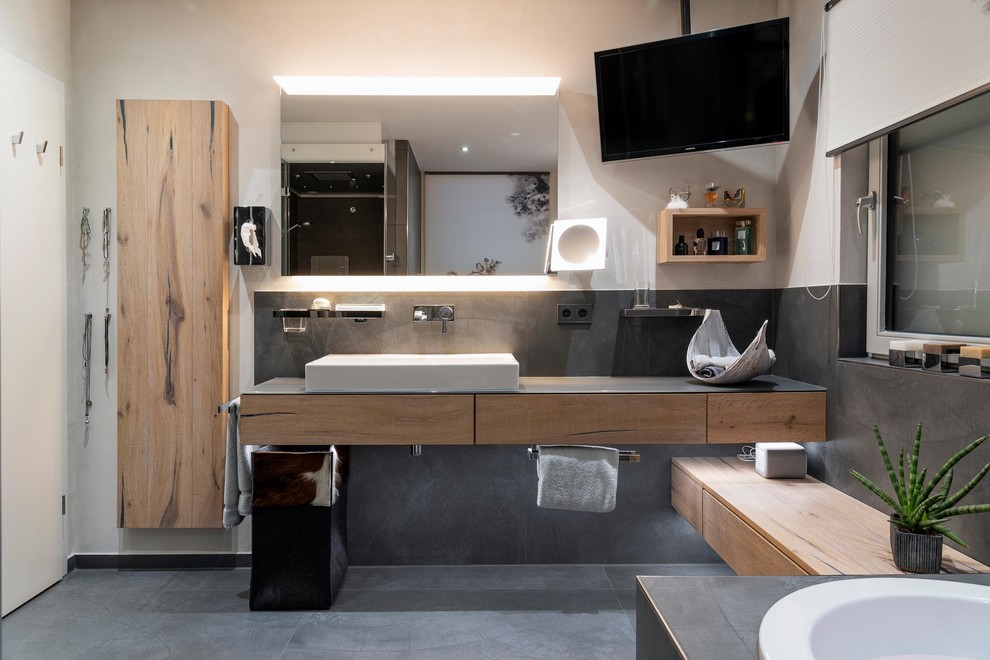 Large contemporary bathroom in Stuttgart with light wood cabinets, a hot tub, a curbless shower, a two-piece toilet, gray tile, stone tile, white walls, ceramic floors, with a sauna, a vessel sink, grey floor, a hinged shower door and brown benchtops.