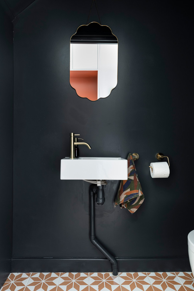 Design ideas for a small eclectic powder room in London with a wall-mount toilet, ceramic floors, a wall-mount sink and red floor.