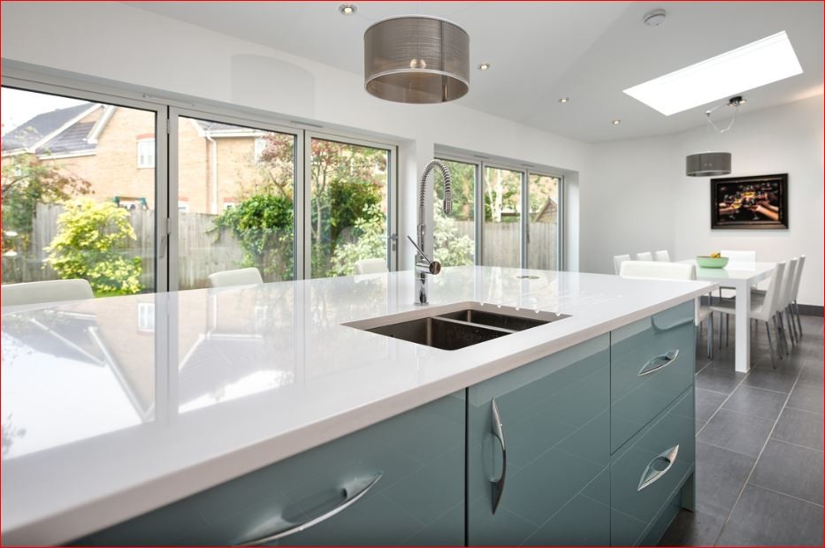This is an example of a mid-sized contemporary l-shaped open plan kitchen in Cambridgeshire with a drop-in sink, flat-panel cabinets, blue cabinets, white splashback, matchstick tile splashback, stainless steel appliances, ceramic floors and with island.