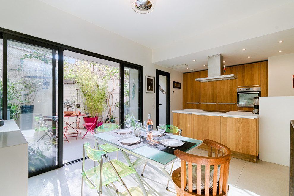 Exemple de cuisine américaine en bois clair avec un évier encastré, un placard à porte plane, un plan de travail en stratifié, une crédence blanche, un électroménager noir, un sol en carrelage de céramique, îlot et un sol beige.