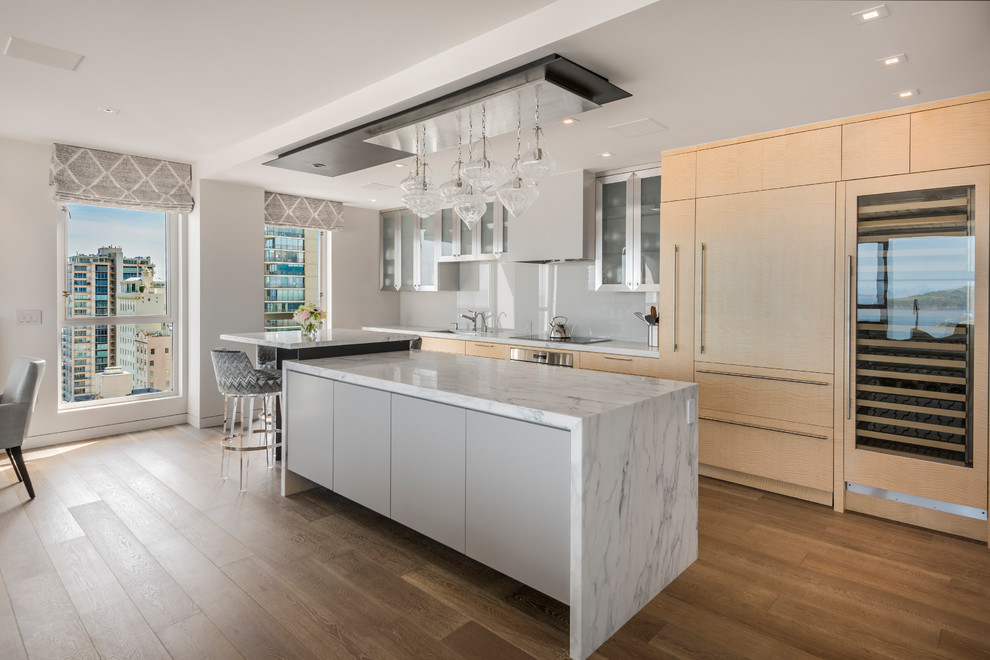 Inspiration for a mid-sized contemporary eat-in kitchen in San Francisco with an undermount sink, flat-panel cabinets, light wood cabinets, marble benchtops, grey splashback, glass sheet splashback, panelled appliances, medium hardwood floors and multiple islands.