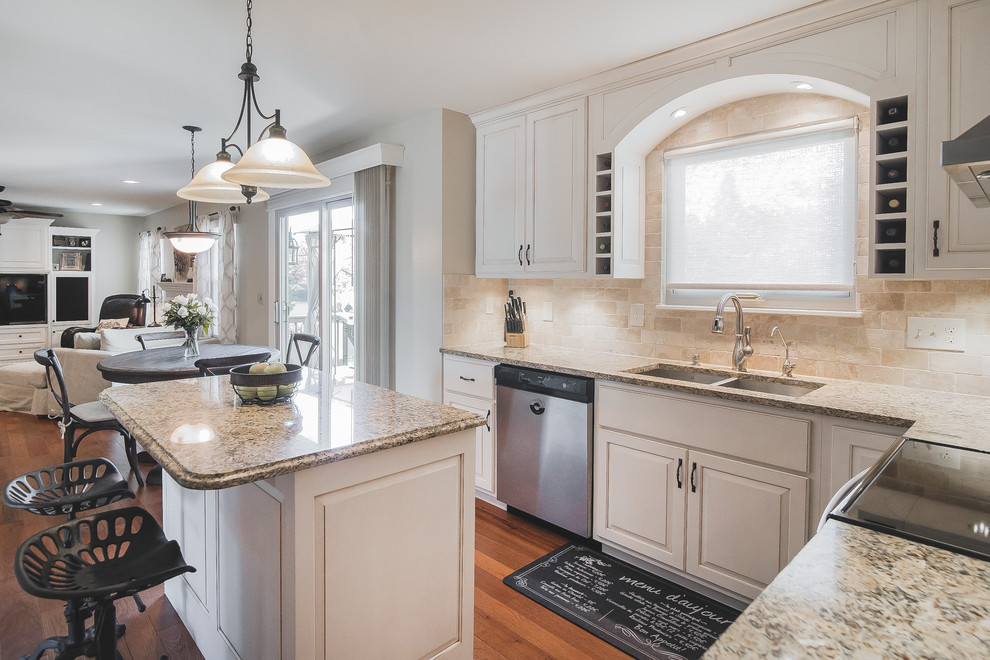 Inspiration for a mid-sized transitional l-shaped open plan kitchen in Columbus with with island, a double-bowl sink, raised-panel cabinets, white cabinets, granite benchtops, beige splashback, stone tile splashback, stainless steel appliances and medium hardwood floors.