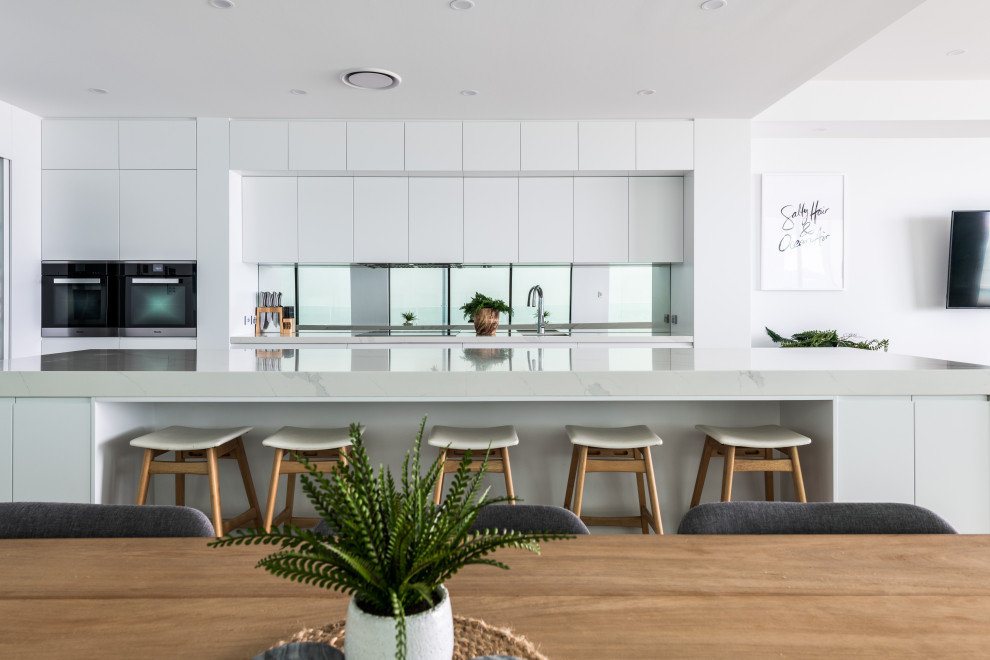 Inspiration for a large contemporary galley open plan kitchen in Gold Coast - Tweed with an undermount sink, flat-panel cabinets, white cabinets, quartz benchtops, mirror splashback, stainless steel appliances, porcelain floors, with island, multi-coloured floor and white benchtop.