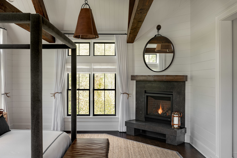 Large farmhouse master dark wood floor and brown floor bedroom photo in New York with white walls, a corner fireplace and a stone fireplace
