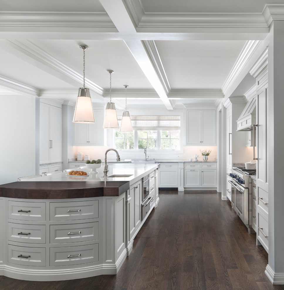 Large transitional l-shaped eat-in kitchen in Detroit with a farmhouse sink, recessed-panel cabinets, white cabinets, white splashback, panelled appliances, dark hardwood floors, with island, brown floor, white benchtop, marble benchtops and subway tile splashback.