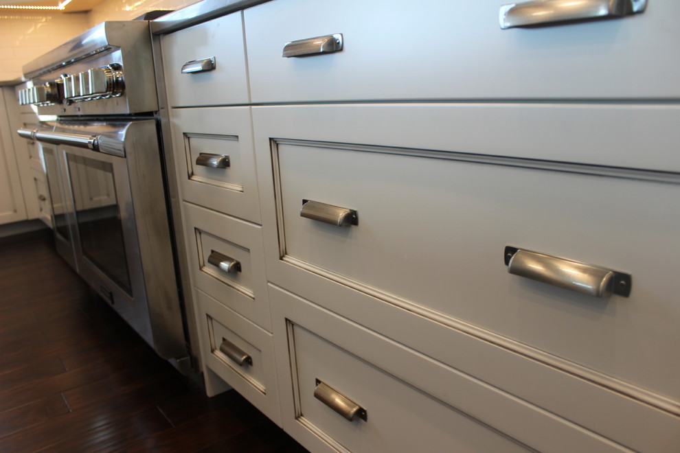 Example of a large transitional l-shaped dark wood floor enclosed kitchen design with a farmhouse sink, shaker cabinets, white cabinets, quartz countertops, white backsplash, subway tile backsplash, stainless steel appliances and an island
