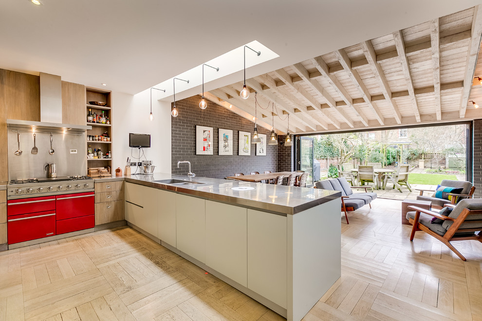 Contemporary l-shaped open plan kitchen in London with a double-bowl sink, flat-panel cabinets, white cabinets, stainless steel benchtops, metallic splashback, coloured appliances, light hardwood floors, a peninsula, beige floor and grey benchtop.