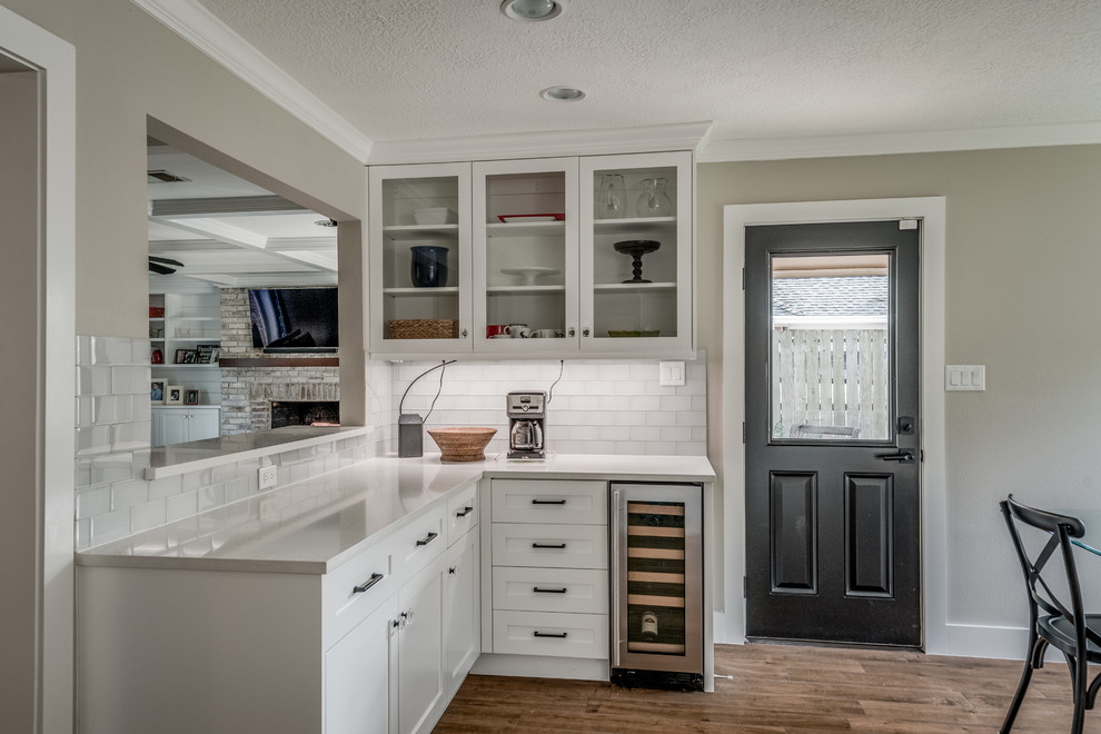 This is an example of a mid-sized traditional l-shaped eat-in kitchen in Houston with a double-bowl sink, shaker cabinets, white cabinets, quartzite benchtops, white splashback, glass tile splashback, stainless steel appliances, porcelain floors, with island, brown floor and white benchtop.