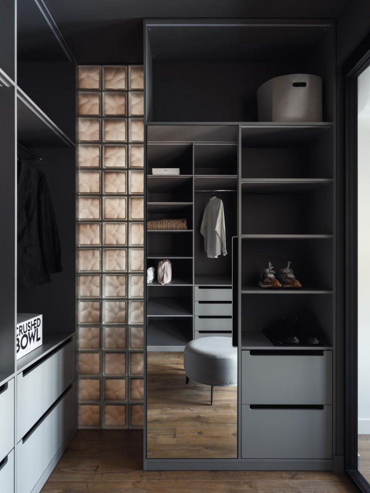 Imagen de armario vestidor unisex urbano grande con armarios con paneles lisos, puertas de armario grises, suelo laminado, suelo marrón y bandeja