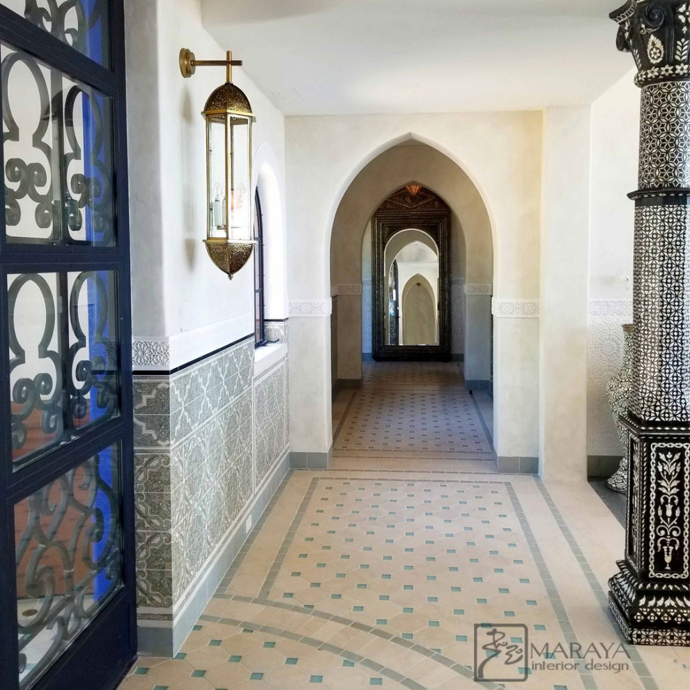 Inspiration for a large mediterranean hallway in Santa Barbara with white walls, limestone flooring, a single front door, a glass front door, white floors, a vaulted ceiling and wainscoting.