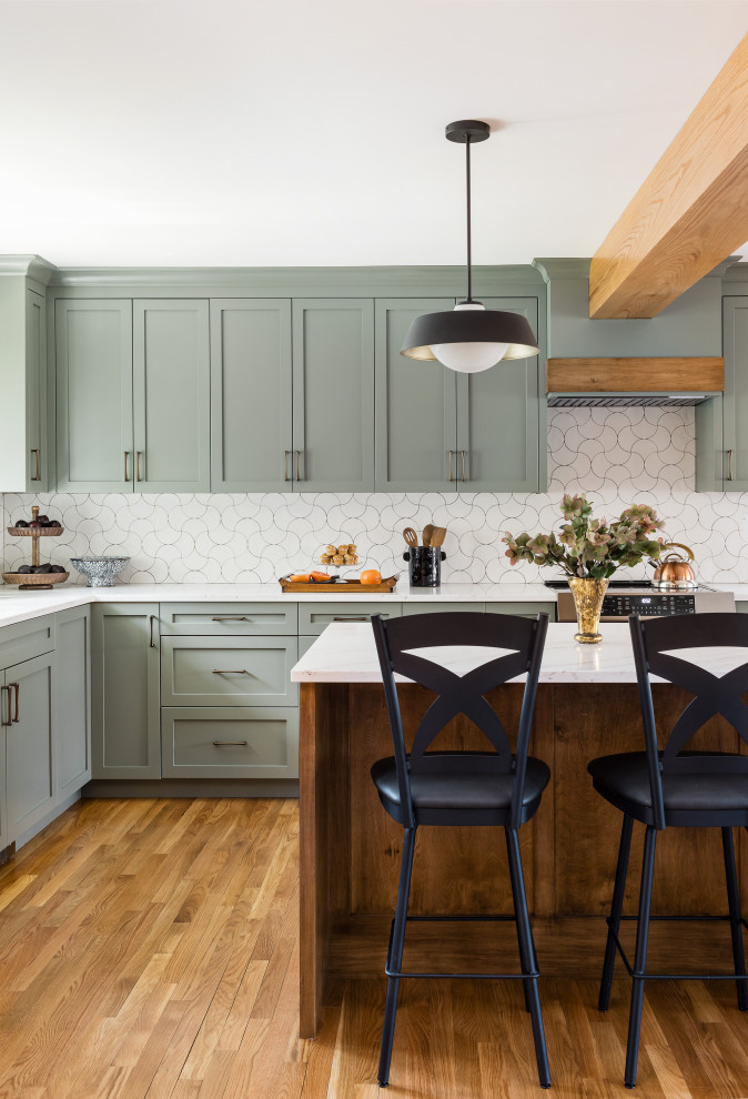 Example of a transitional medium tone wood floor and brown floor kitchen design in Boston with an undermount sink, shaker cabinets, green cabinets, porcelain backsplash, an island, quartz countertops, white backsplash, stainless steel appliances and white countertops