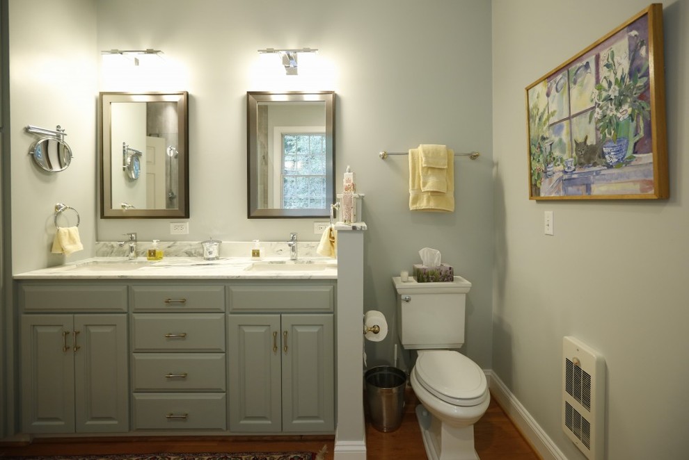 This is an example of a mid-sized transitional master bathroom in San Diego with raised-panel cabinets, grey cabinets, a drop-in tub, a corner shower, a one-piece toilet, white tile, white walls, light hardwood floors, an undermount sink and marble benchtops.