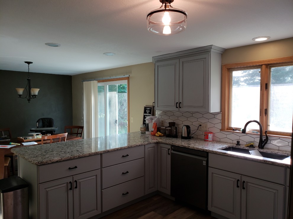 Example of a mid-sized transitional u-shaped medium tone wood floor and brown floor eat-in kitchen design with an undermount sink, raised-panel cabinets, gray cabinets, granite countertops, white backsplash, ceramic backsplash, stainless steel appliances, a peninsula and multicolored countertops
