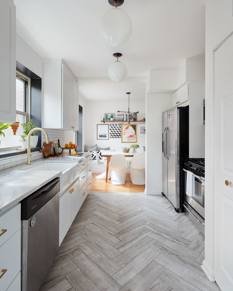Photo of a mid-sized transitional galley eat-in kitchen in Chicago with a farmhouse sink, flat-panel cabinets, white cabinets, marble benchtops, white splashback, porcelain splashback, stainless steel appliances, travertine floors, no island and grey floor.