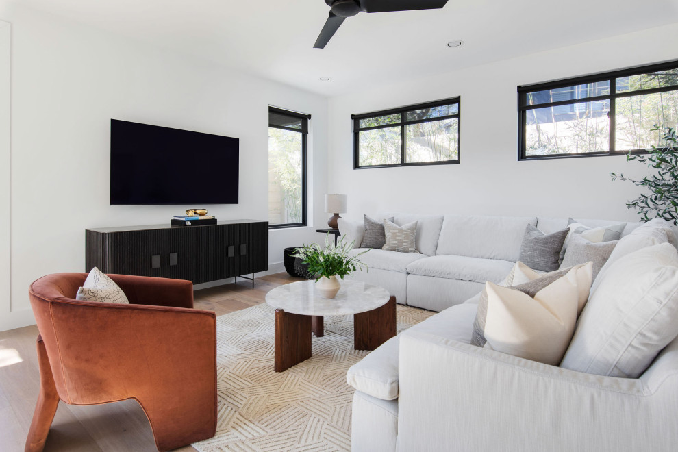 Ejemplo de salón abierto actual de tamaño medio con paredes blancas, suelo de madera clara, televisor colgado en la pared y suelo beige