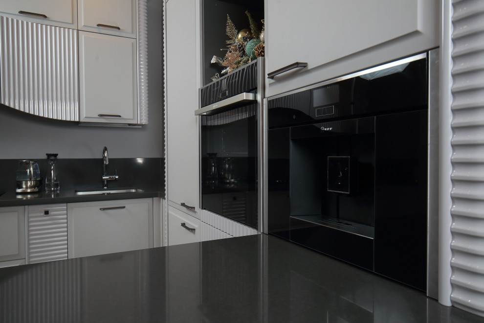 Bild på ett stort funkis svart svart kök, med en enkel diskho, luckor med upphöjd panel, grå skåp, bänkskiva i kvarts, svart stänkskydd, svarta vitvaror, klinkergolv i porslin, en köksö och beiget golv