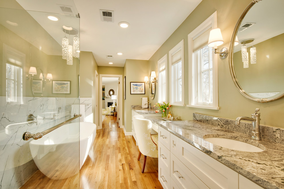 Design ideas for an expansive transitional master bathroom in Kansas City with shaker cabinets, white cabinets, a freestanding tub, a two-piece toilet, green tile, ceramic tile, green walls, medium hardwood floors, an undermount sink, granite benchtops, brown floor and a hinged shower door.