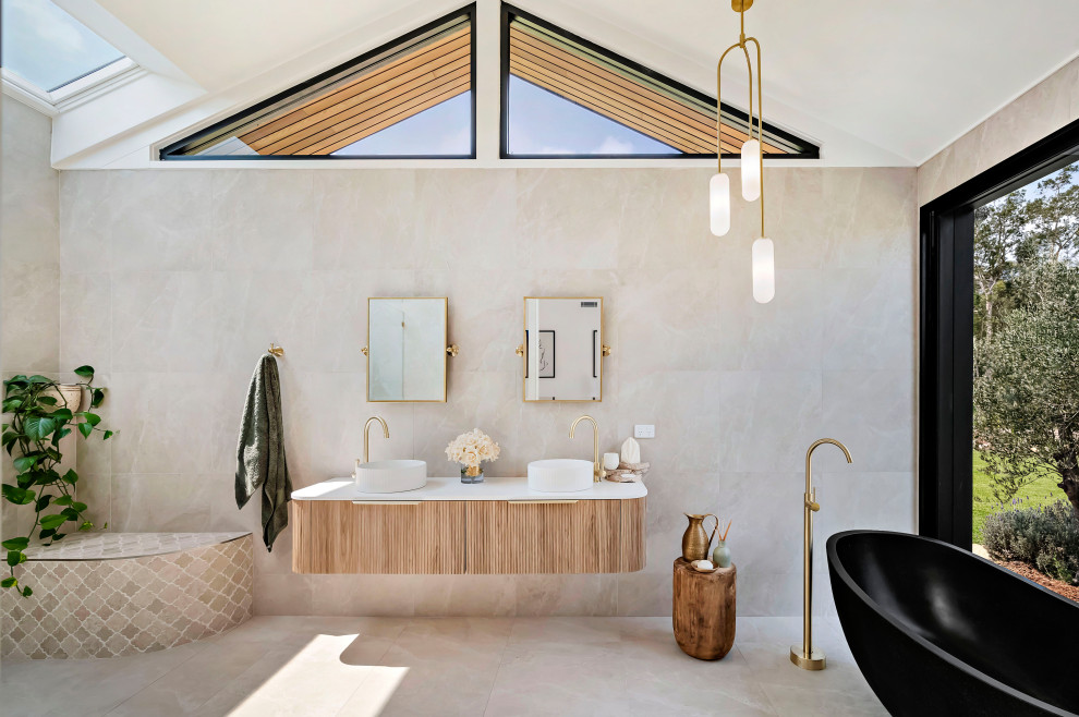 This is an example of an expansive contemporary master bathroom in Central Coast with a freestanding tub, a vessel sink, engineered quartz benchtops, an open shower, white benchtops, a double vanity, a floating vanity, flat-panel cabinets, light wood cabinets, a curbless shower, beige tile, beige floor, a shower seat and vaulted.