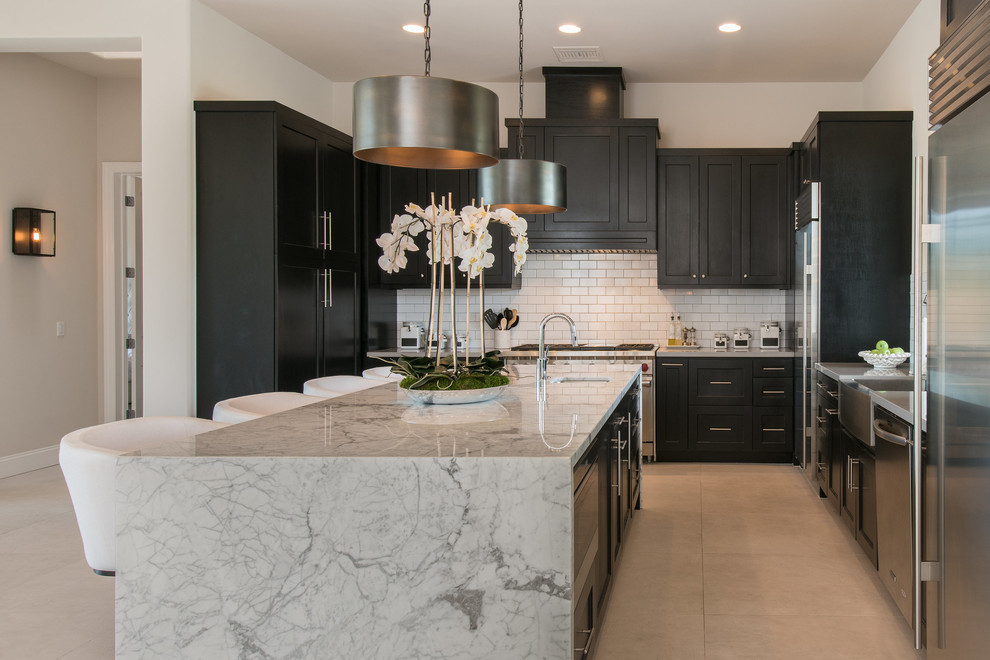 Inspiration for a transitional u-shaped kitchen in Phoenix with a farmhouse sink, shaker cabinets, black cabinets, white splashback, subway tile splashback, stainless steel appliances, with island, grey floor and white benchtop.