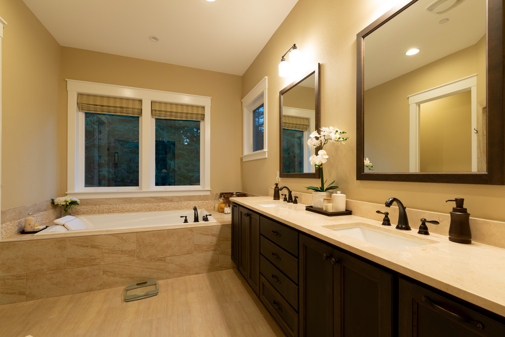 This is an example of a large traditional master wet room bathroom in Portland with dark wood cabinets, a drop-in tub, brown tile, stone tile, beige walls, light hardwood floors, an undermount sink, granite benchtops, beige floor, a hinged shower door and beige benchtops.