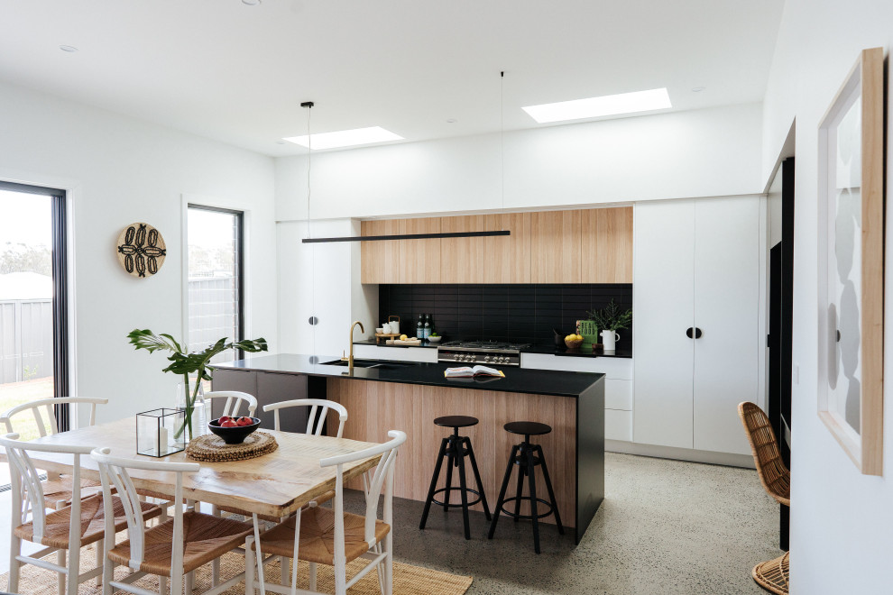 Design ideas for a mid-sized modern galley open plan kitchen in Wollongong with an undermount sink, flat-panel cabinets, black cabinets, quartz benchtops, black splashback, ceramic splashback, stainless steel appliances, concrete floors, with island, grey floor and black benchtop.