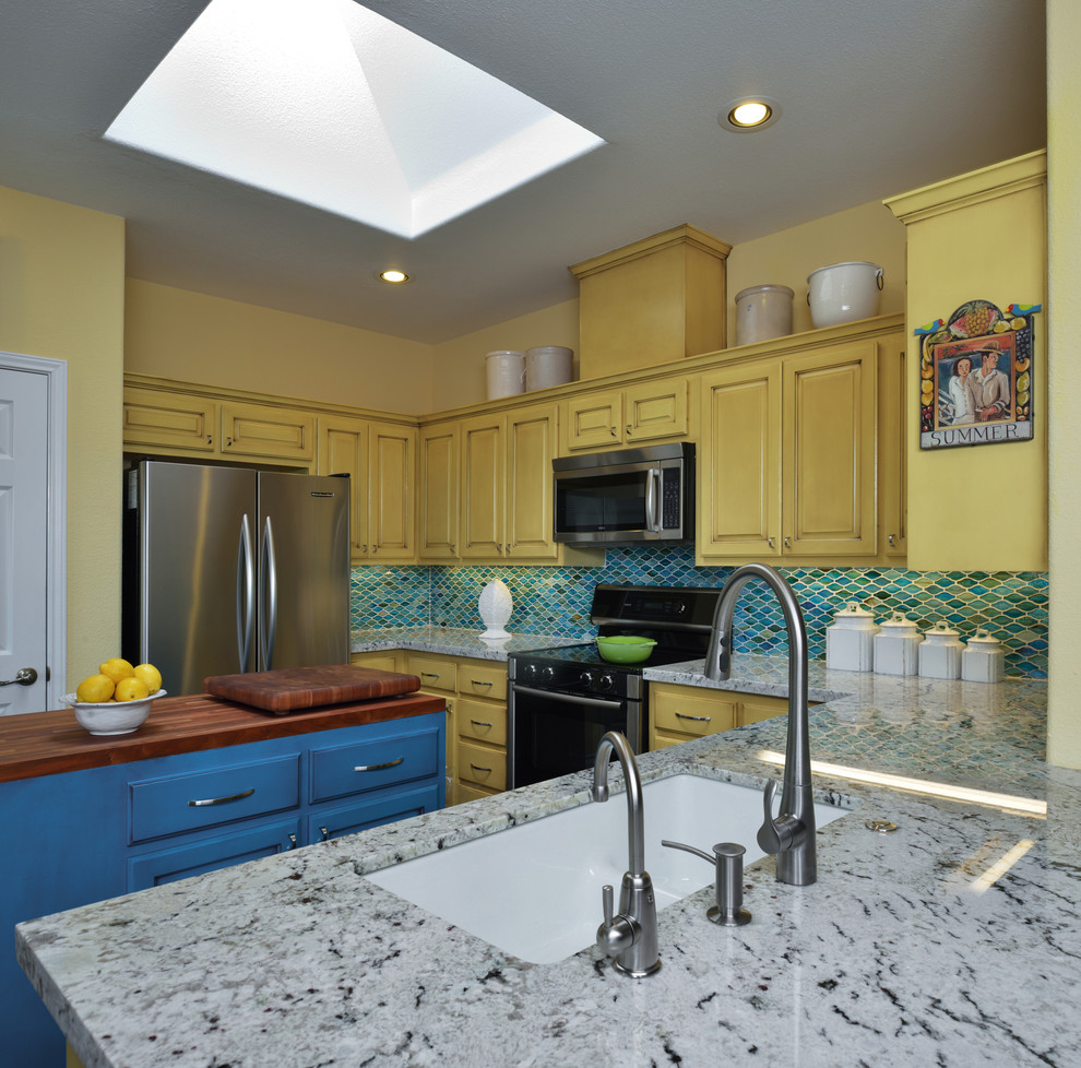 This is an example of a mid-sized traditional u-shaped open plan kitchen in Austin with an undermount sink, raised-panel cabinets, yellow cabinets, granite benchtops, blue splashback, stainless steel appliances and with island.