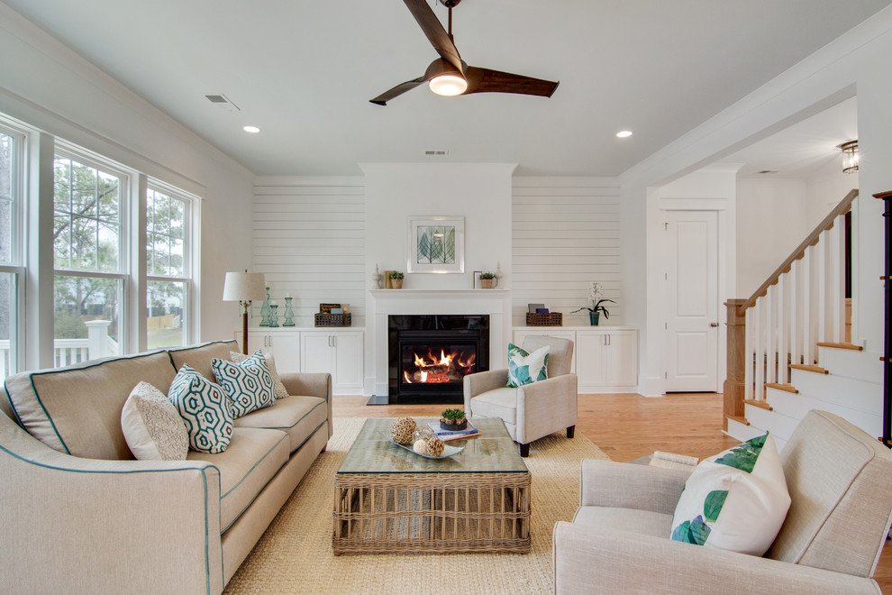 Photo of a beach style living room in Charleston with light hardwood floors, white walls, a standard fireplace, no tv and beige floor.