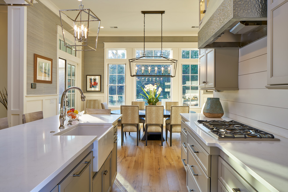 This is an example of a mid-sized transitional single-wall eat-in kitchen in Charleston with a farmhouse sink, shaker cabinets, grey cabinets, granite benchtops, white splashback, timber splashback, stainless steel appliances, light hardwood floors, with island, brown floor and white benchtop.